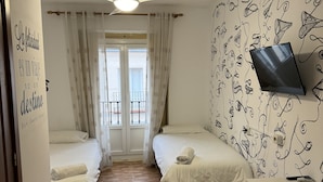 A hotel room with two beds, a ceiling fan, a TV, and a wall with a unique pattern. - Residencia Rosales (Madrid)