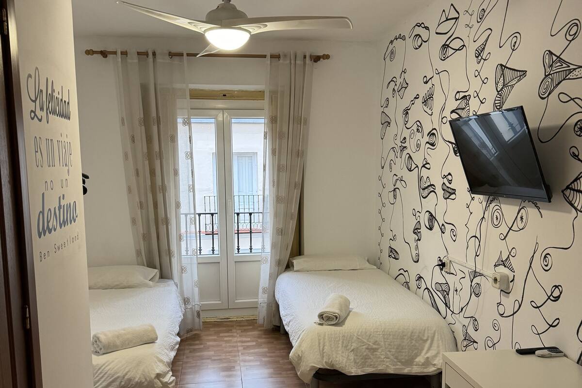 Habitación de hotel con dos camas, un ventilador de techo, un televisor y una pared con un diseño original.