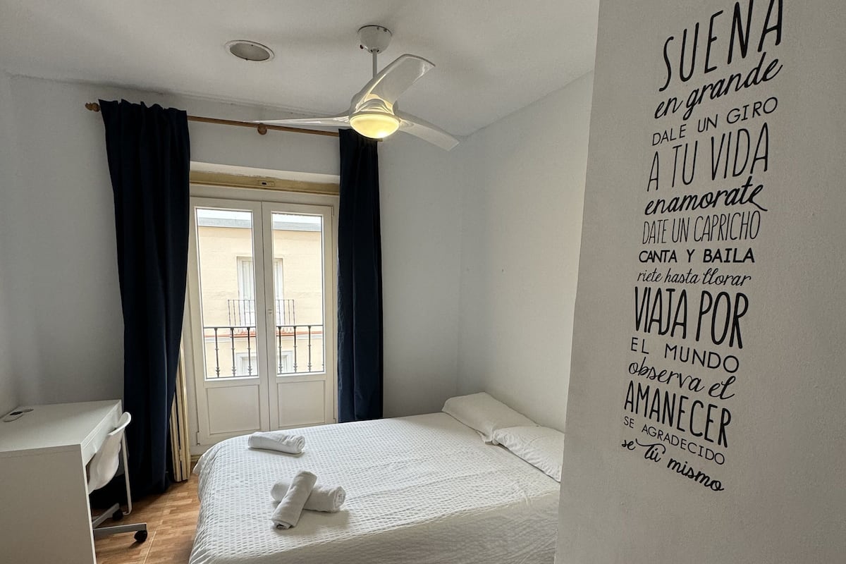 Habitación de hotel con dos camas, un escritorio y un ventilador de techo.