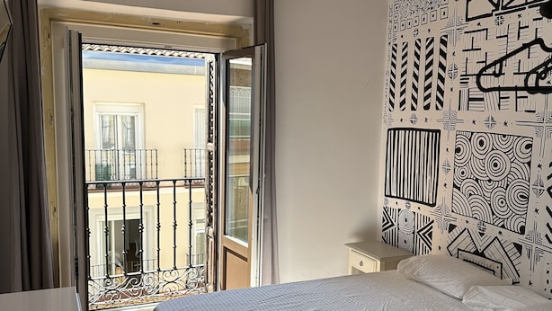 A hotel room with a bed, a desk, a balcony with a view, and a ceiling fan. - Residencia Rosales (Madrid)