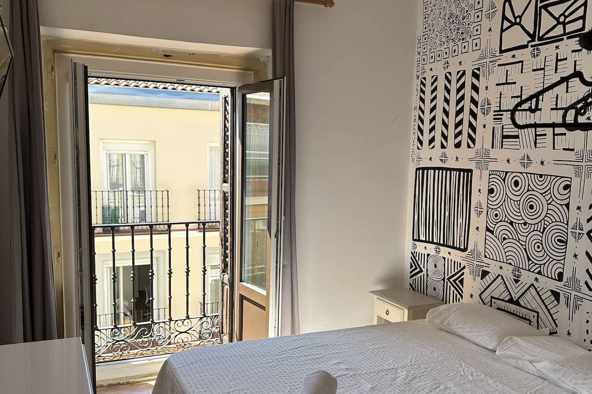 Habitación de hotel con cama, escritorio, balcón con vistas y ventilador de techo.