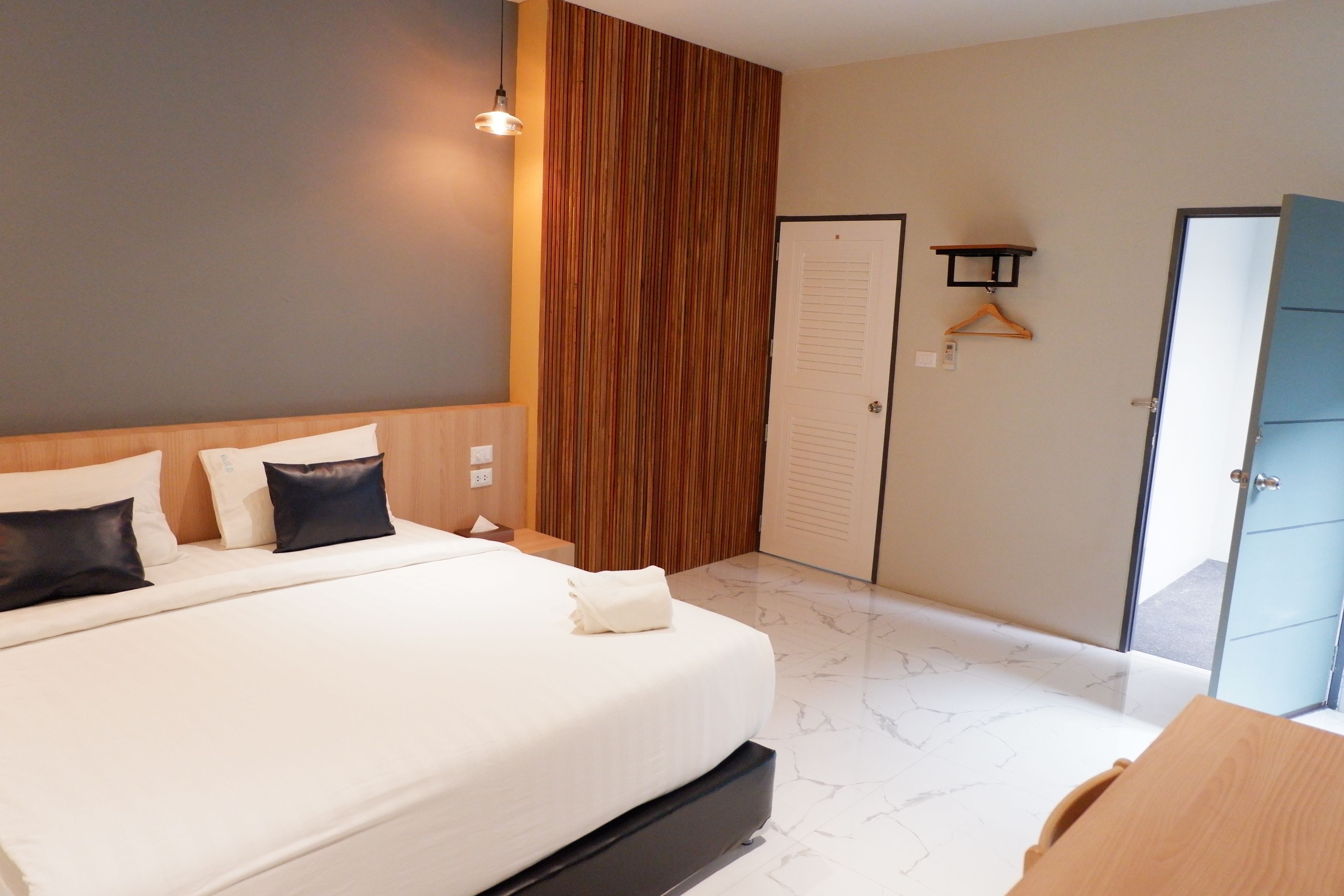 Un dormitorio moderno con una cama grande, cabecera de madera, lámpara colgante, armario y una puerta con perchero.