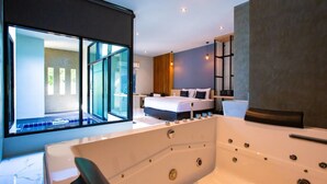 A modern hotel room with a large bathtub, a bed with white linens, and a large window offering a view of the pool area. - Chill D Resort (Buriram)