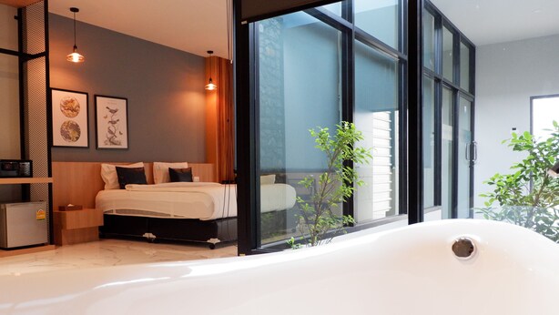 A modern bedroom with a large window, a bathtub, and a bed with white bedding. - Chill D Resort (Buriram)