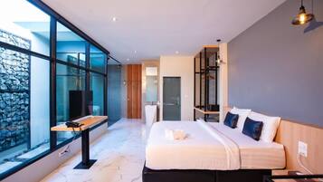 A modern bedroom with a large bed, a desk, and a view of a stone wall through large windows.