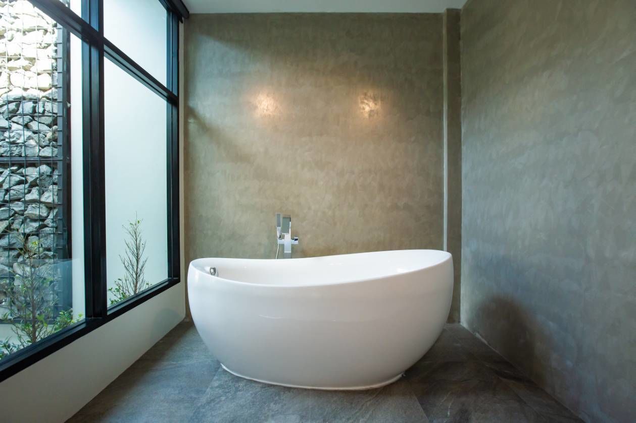 A modern bathroom with a freestanding bathtub, large windows, and a stone wall.