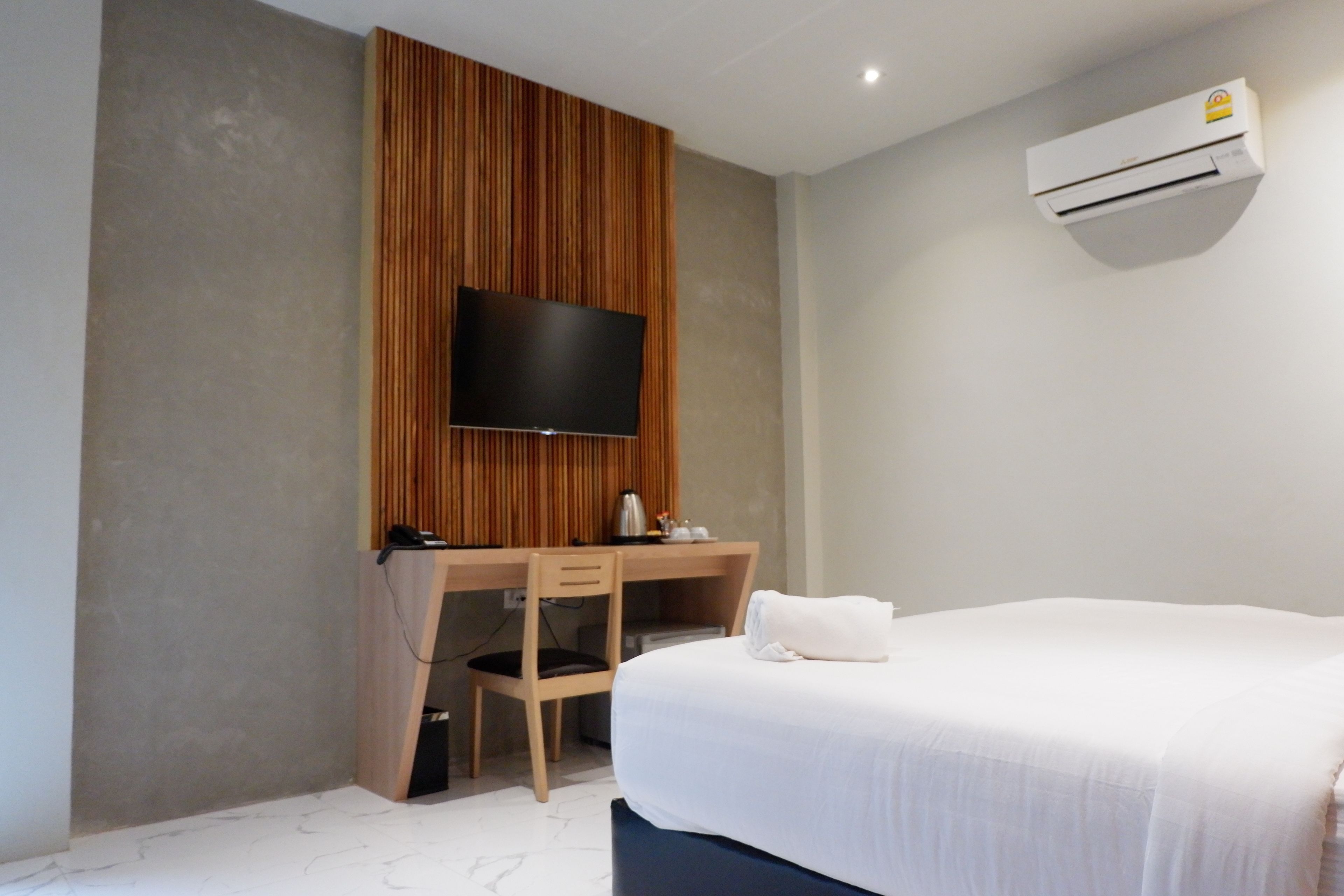 A modern hotel room with a large bed, a wooden desk with a flat-screen TV, a chair, and a small table with a kettle.