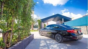 A black car parked in front of a modern building with a stone facade and a blue awning. - Chill D Resort (Buriram)