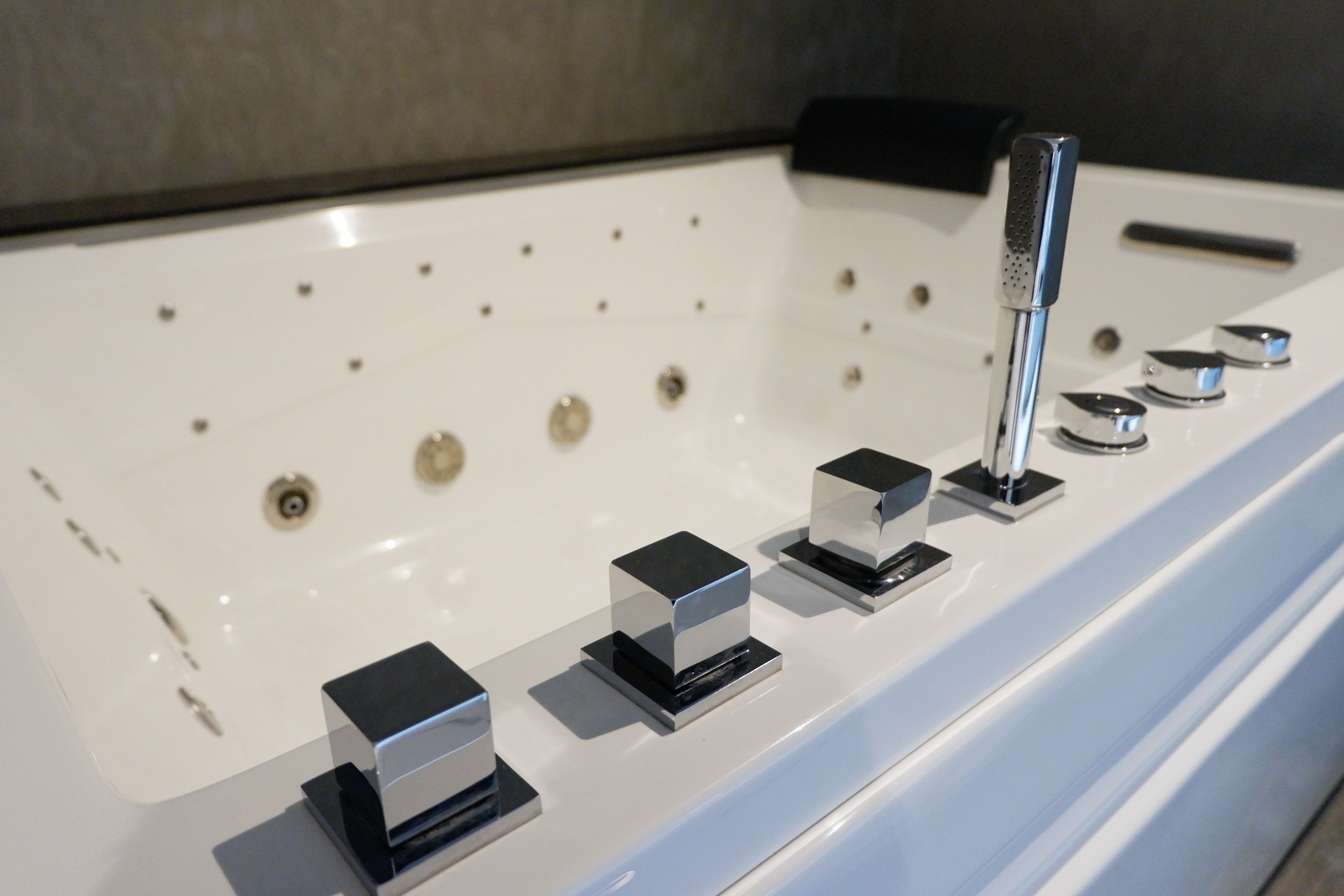 A modern bathroom with a white bathtub, multiple control knobs, and a handheld showerhead.