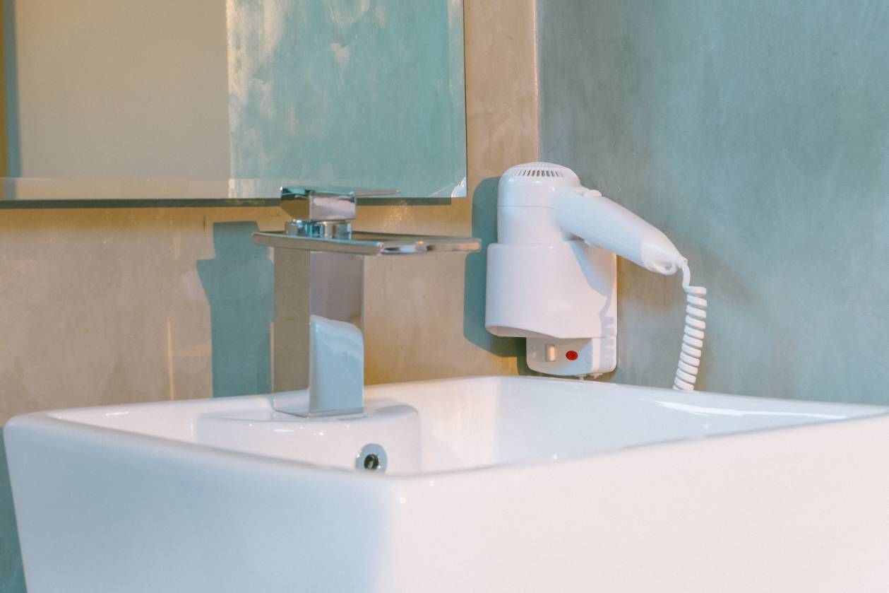 A white sink with a hairdryer mounted on the wall above it.