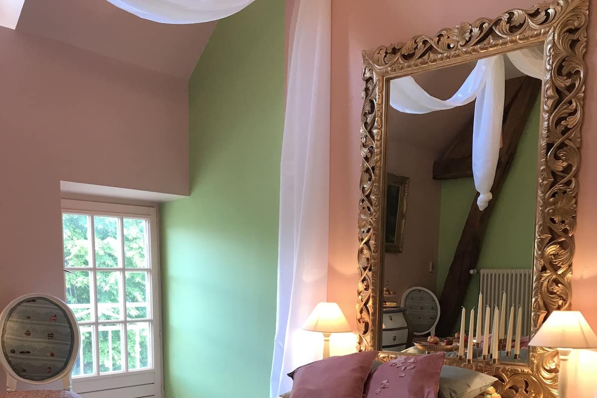 Un dormitorio con una cama, dos lámparas de noche, un espejo, una silla y una ventana.