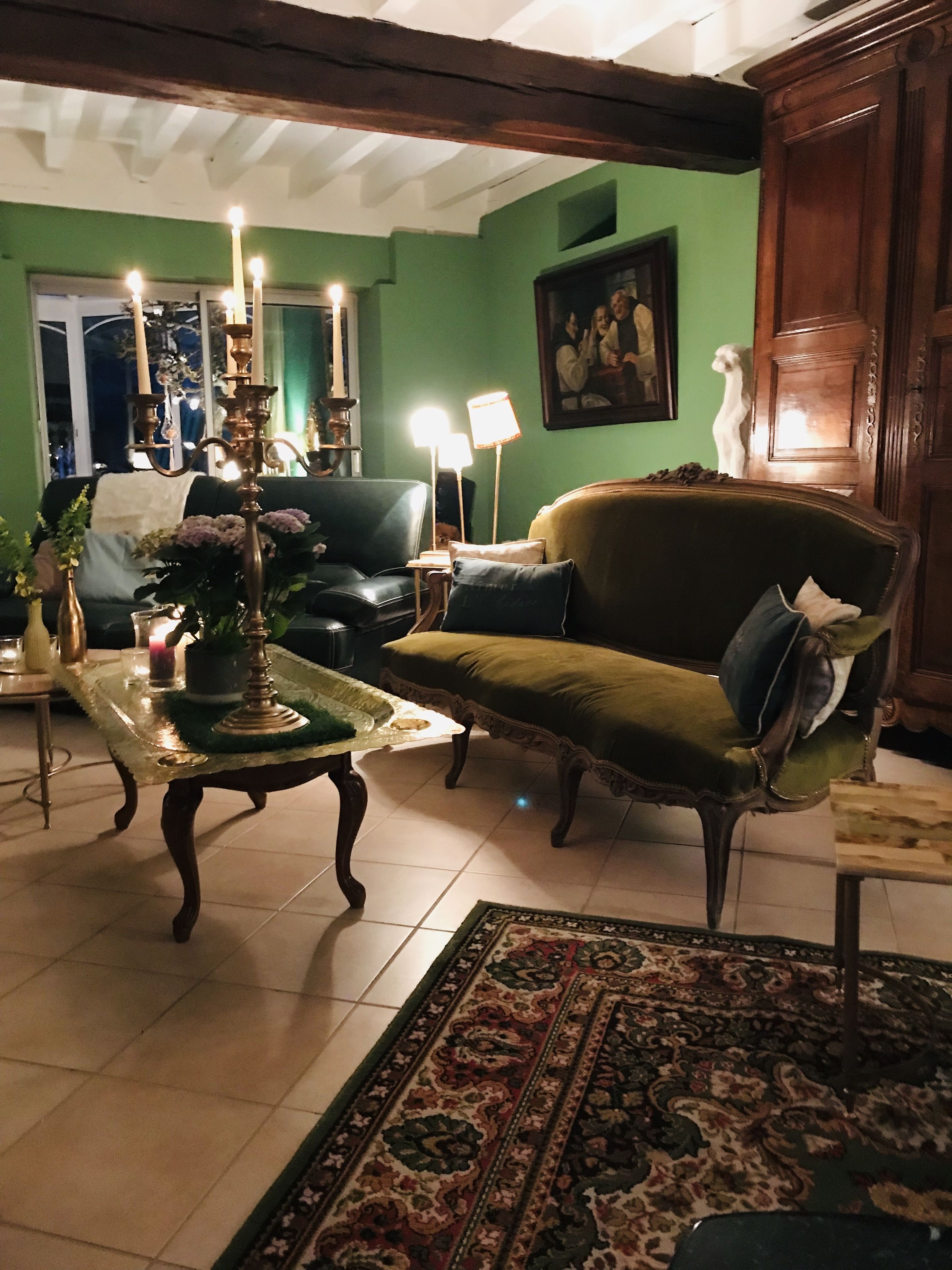 Una sala de estar con un sofá verde, un tapete estampado y un candelabro.