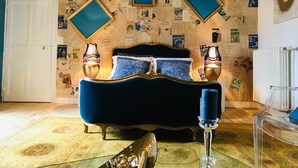 Un dormitorio con una cama tapizada en azul, dos lámparas fijadas a la pared y una alfombra estampada.