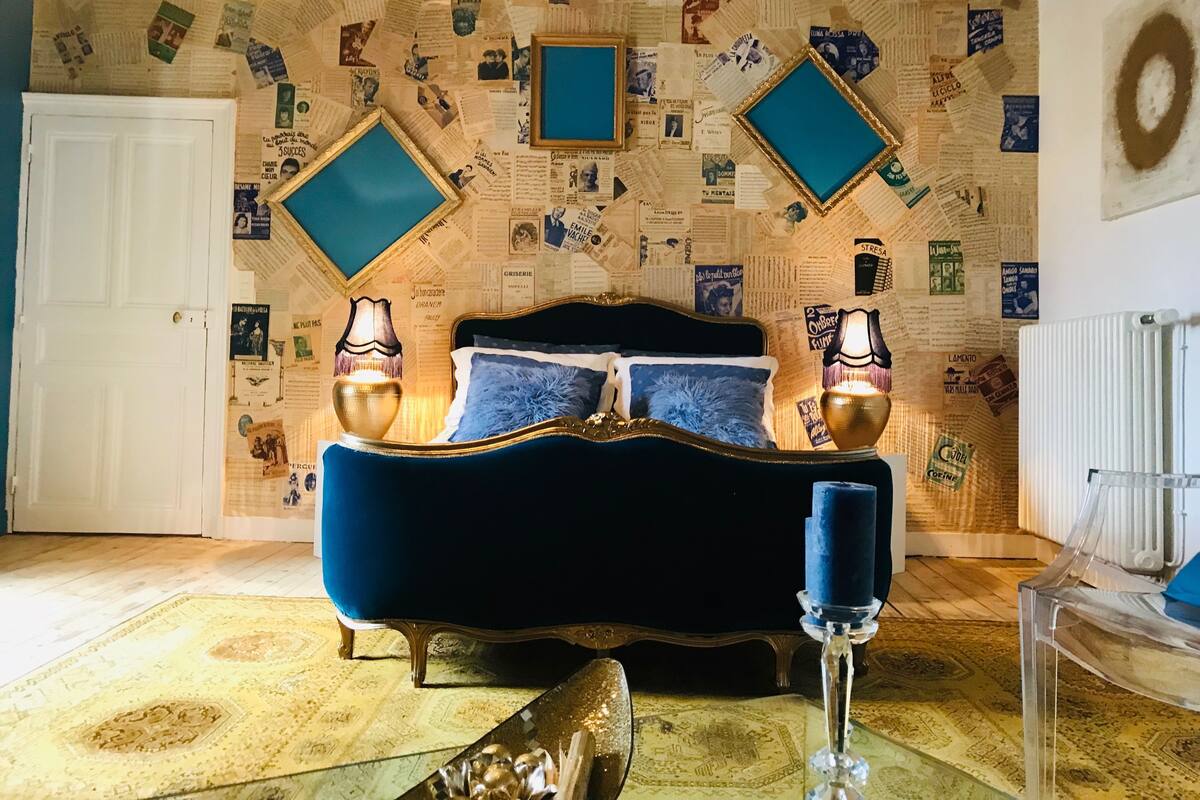 Un dormitorio con una cama tapizada en azul, dos lámparas fijadas a la pared y una alfombra estampada.