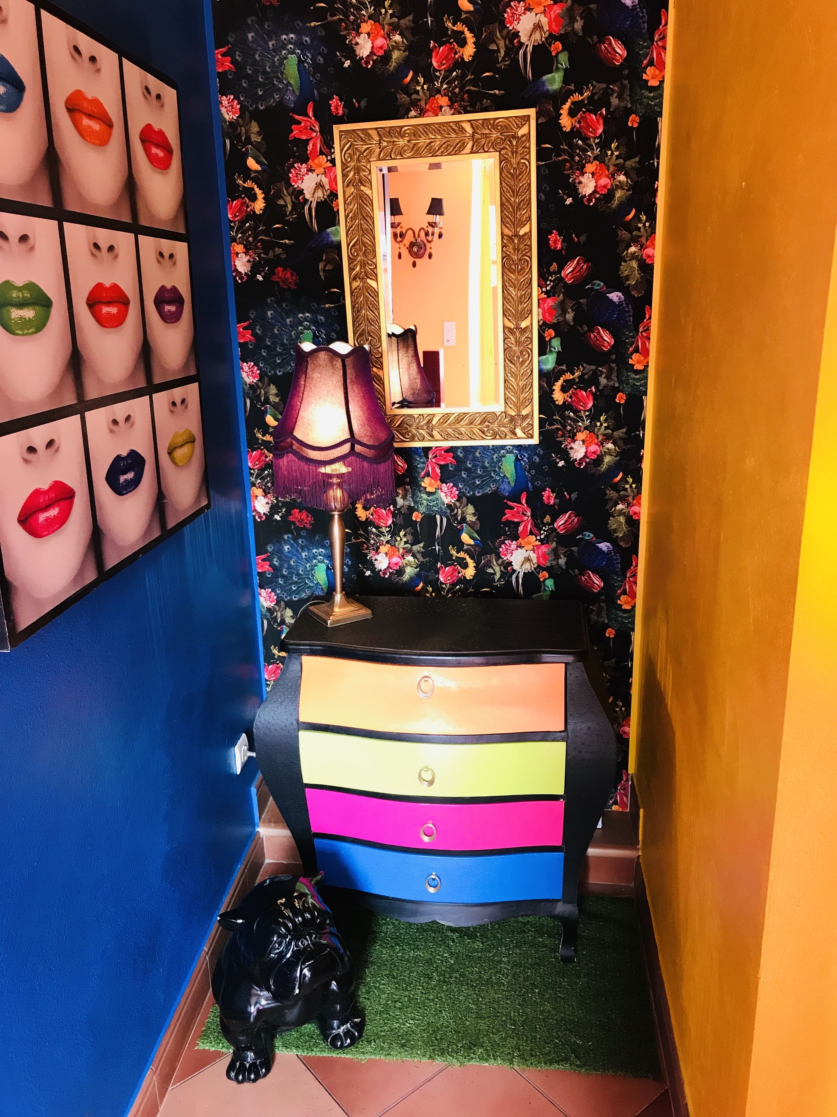 A room with a mirror, a lamp, a dresser, and a black cat statue.