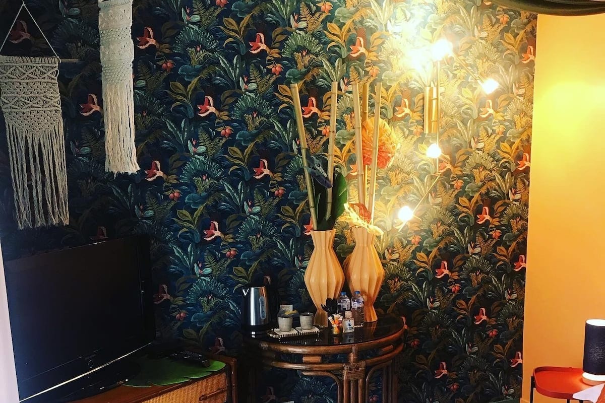 Una habitación con cama, cómoda, una mesita con hervidor y una pared con estampado floral.