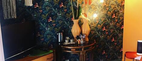 Una habitación con cama, cómoda, una mesita con hervidor y una pared con estampado floral.