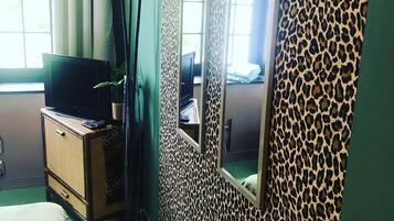 Ein Zimmer mit Wand in Leopardenmuster, einem Fernseher auf einer Holzkommode und einem Fenster mit Vorhängen.