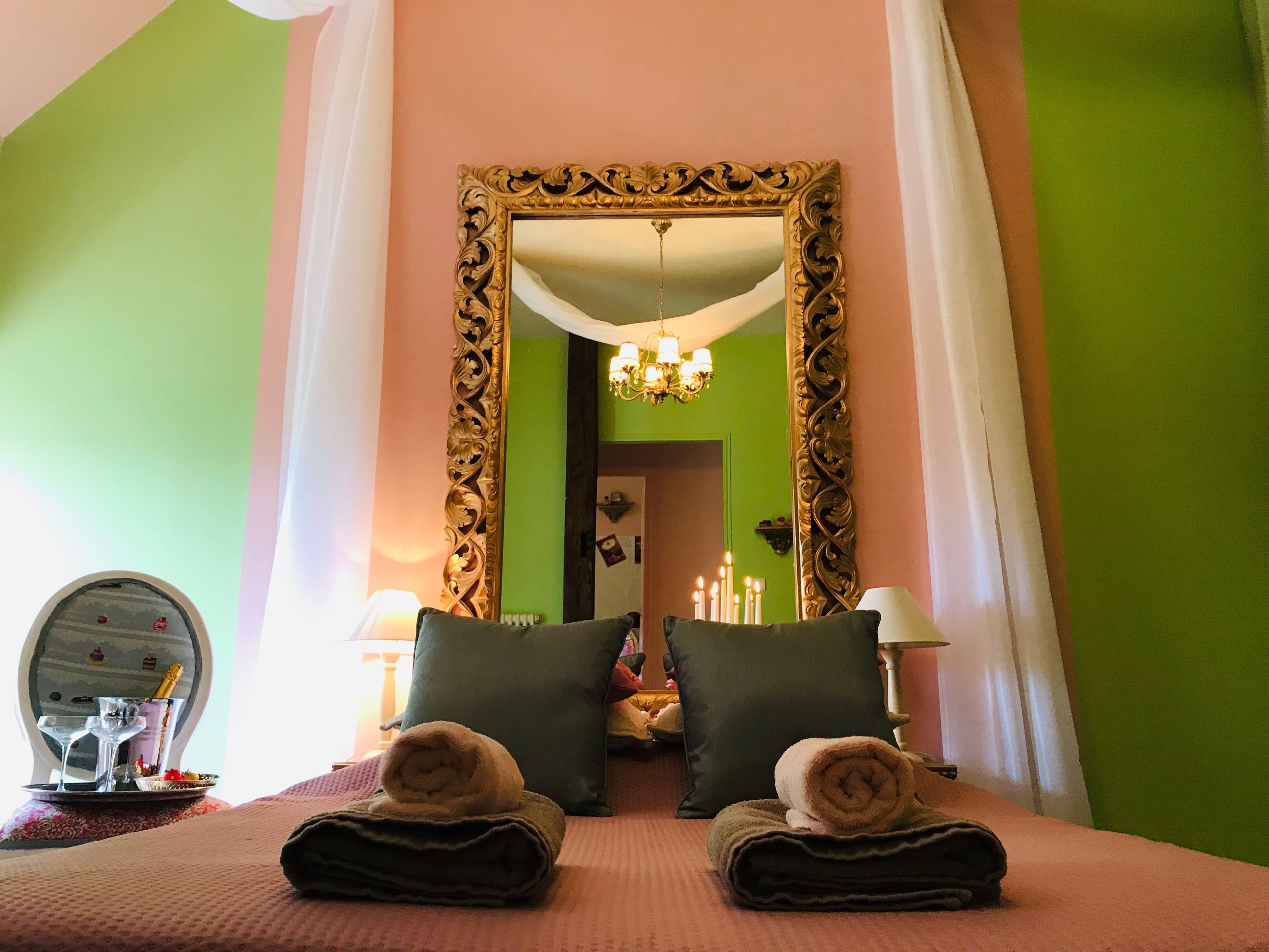 Habitación de hotel con cama, dos almohadas, espejo, mesita de noche con lámpara y marco decorativo para espejo.