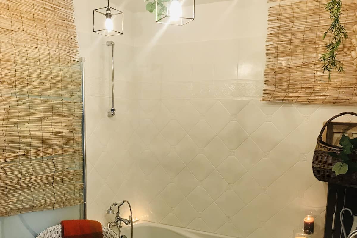 Un baño con una bañera, un lavabo blanco y una silla de mimbre con toallas.