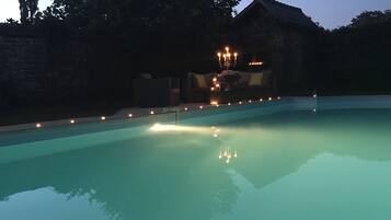 Piscina com borda de pedra, rodeada por um muro baixo e um muro de pedra ao fundo.