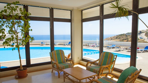 A room with large windows overlooking a pool and beach, wicker furniture, and a potted plant. - A08 - Magnólia Sea View Apartment by DreamAlgarve (Lagos)