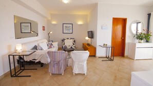 A well-lit living room with a sofa, armchairs, a coffee table, and a TV. There are framed pictures on the walls, a wooden door, and a small table with a plant. - A08 - Magnólia Sea View Apartment by DreamAlgarve (Lagos)