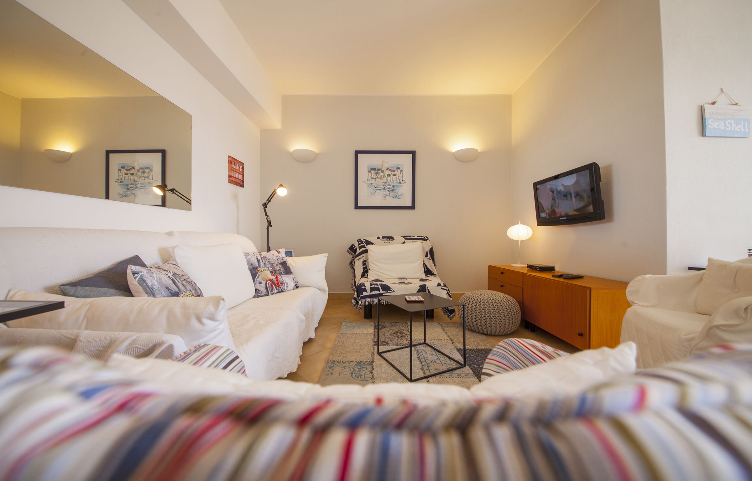 Habitación de hotel con dos camas, un sofá, una mesita, una silla, un televisor y obras de arte en las paredes.