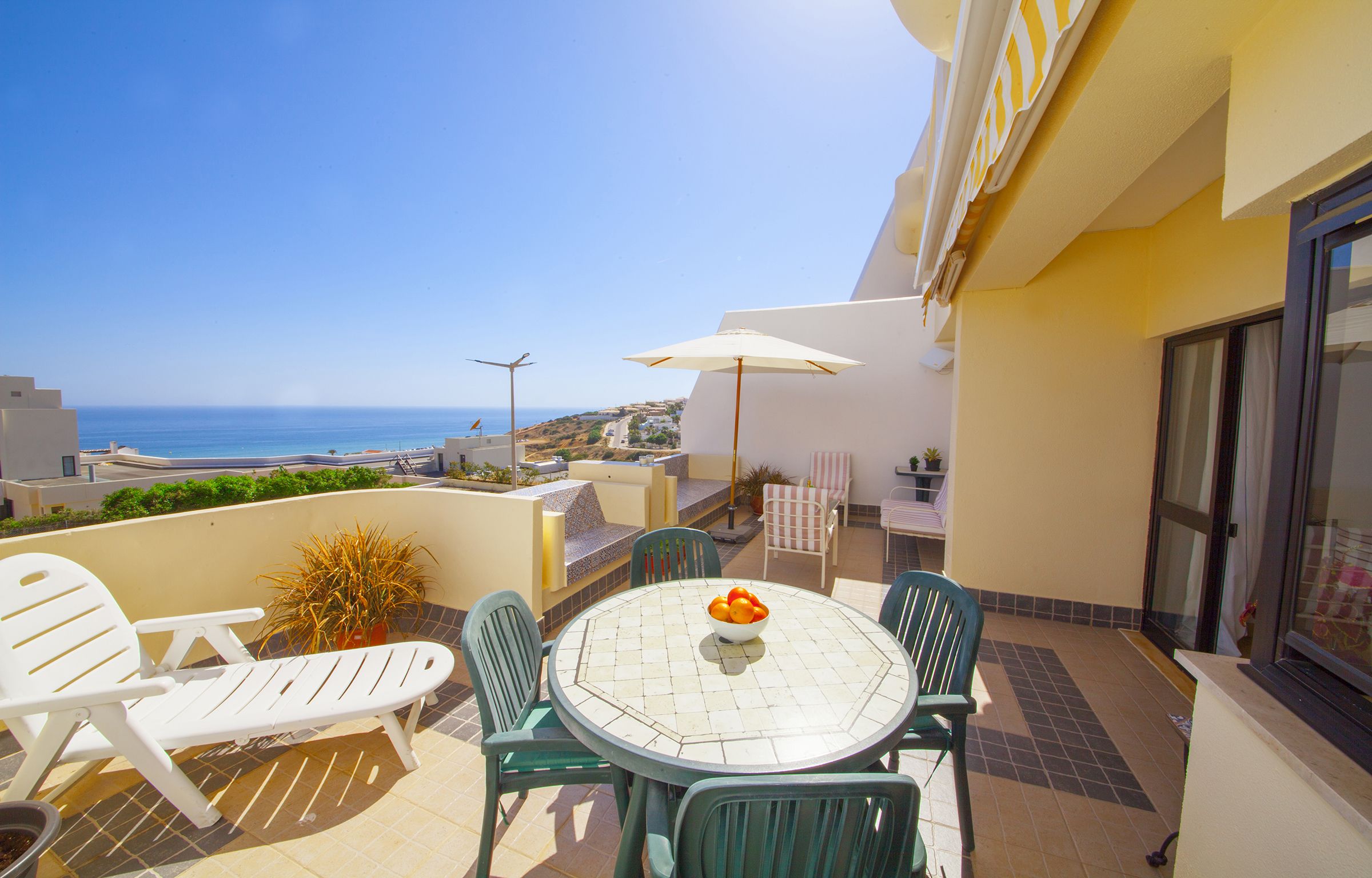 A balcony with a table, chairs, and a bowl of fruit.