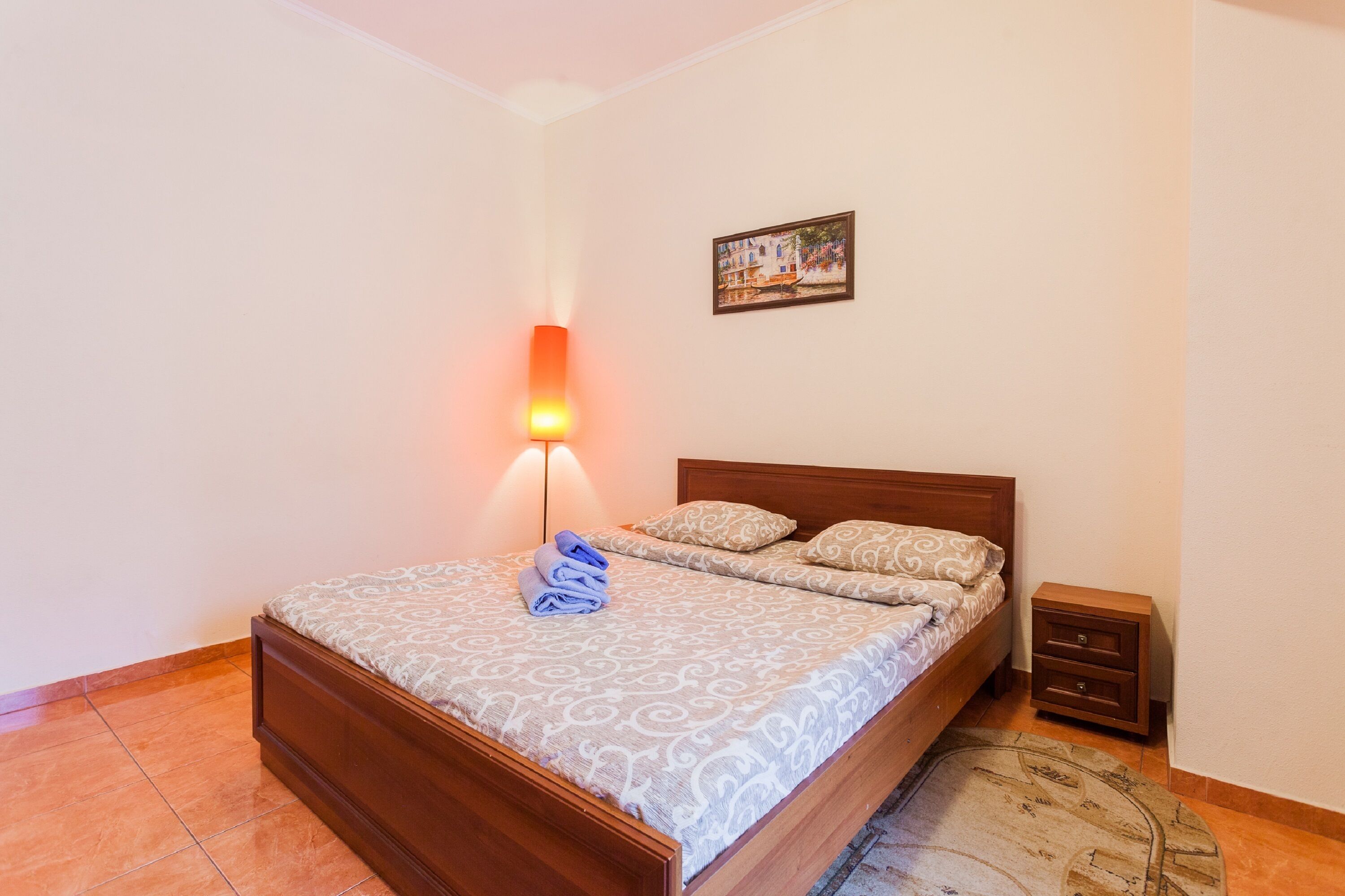 Una cama bien hecha con ropa de cama estampada, una mesita de noche con cajones, una lámpara de pared y un cuadro en la pared.