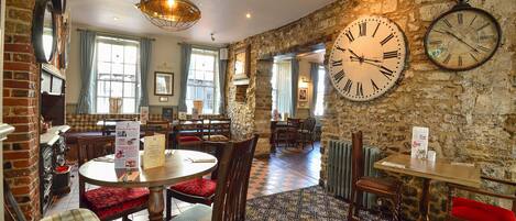A restaurant with stone walls, wooden furniture, and a large clock.