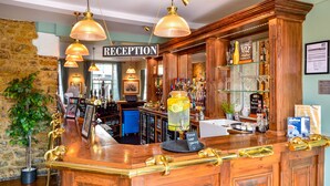 A reception area with a wooden counter, brass fixtures, and a large sign reading "RECEPTION". - The George Hotel (Axminster)