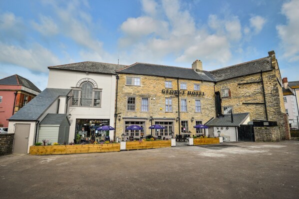 A George Hotel with a stone facade, multiple windows, and outdoor seating with umbrellas.