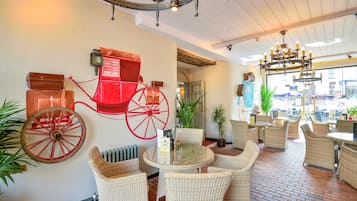 Interior de restaurante con mobiliario de mimbre, una rueda de carruaje roja y un candelabro.