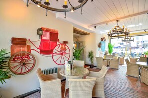 A restaurant interior with wicker furniture, a red carriage wheel, and a chandelier.