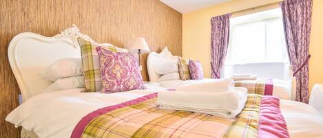 A hotel room with a large bed, multiple pillows, a plaid bedspread, and a window with curtains.