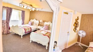 A bedroom with two beds, a mirror, a bedside table, a fan, and a wall-mounted decoration. - The George Hotel (Axminster)