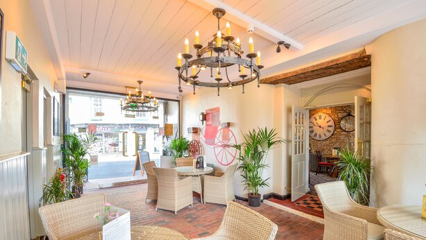 A cozy interior with wicker furniture, a chandelier, and a large wall clock. - The George Hotel (Axminster)