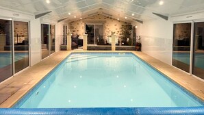An indoor swimming pool with clear glass walls, a tiled floor, and a stone wall with plants. - La Petite Félixière, B&B indépendants à 10 min de Cholet, 25 min du Puy du Fou et 35 min de Nantes (Sèvremoine)