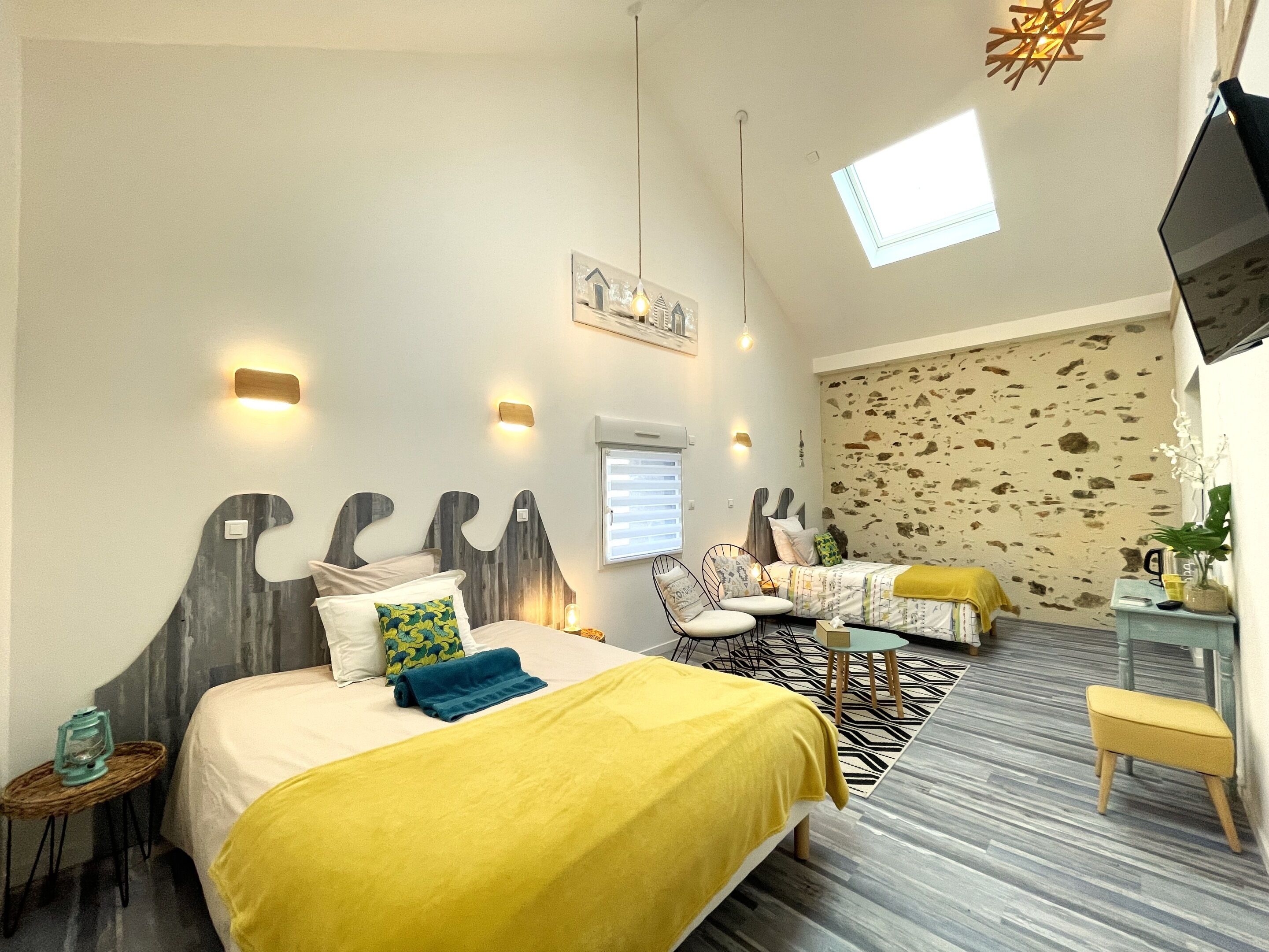 Quarto de hotel com uma cama, escrivaninha, cadeira, mesinha, televisão e janela.