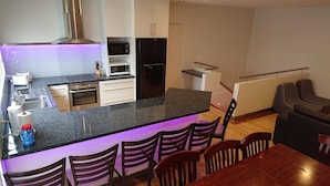 A compact kitchen with a central island, built-in appliances, and a dining area with chairs. - Paradise Escapes - 001 (Cowes)