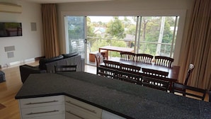 A modern kitchen with a large island, a dining area with wooden furniture, and a sliding glass door leading to an outdoor patio. - Paradise Escapes - 001 (Cowes)