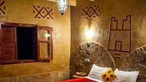 Una habitación con cama, ventana con contraventanas de madera y decoración en la pared.