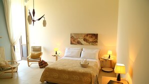 A hotel room with a bed, two bedside lamps, a laptop on the nightstand, a chair, a small table with a lamp, and a painting on the wall. - Balcone su Otranto (Otranto)