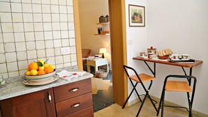 A compact kitchen with a fruit bowl on the counter, a small dining table with chairs, and a doorway leading to a living area. - Balcone su Otranto (Otranto)