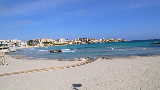 A beach with a clear view of the coastline, buildings in the background, and a sandy shore. - Balcone su Otranto (Otranto)