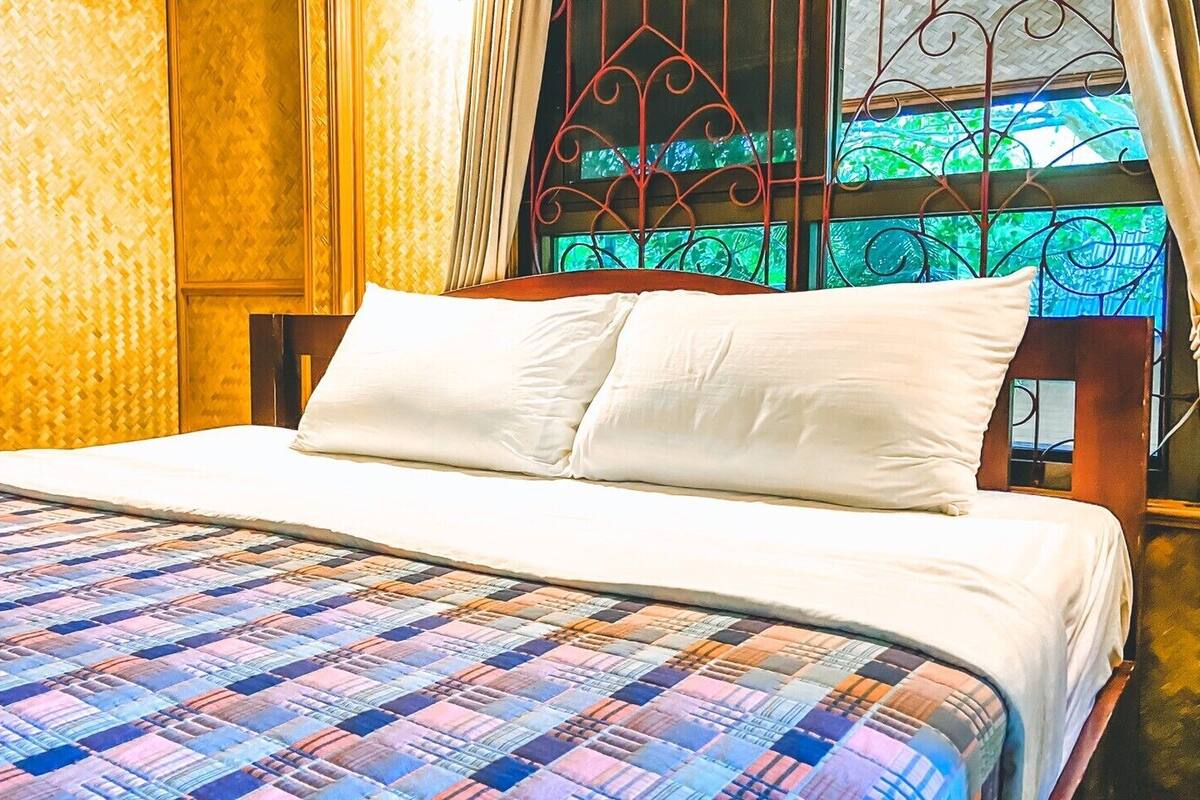 Una cama con colcha, una ventana con diseño metálico y un papel tapiz estampado.