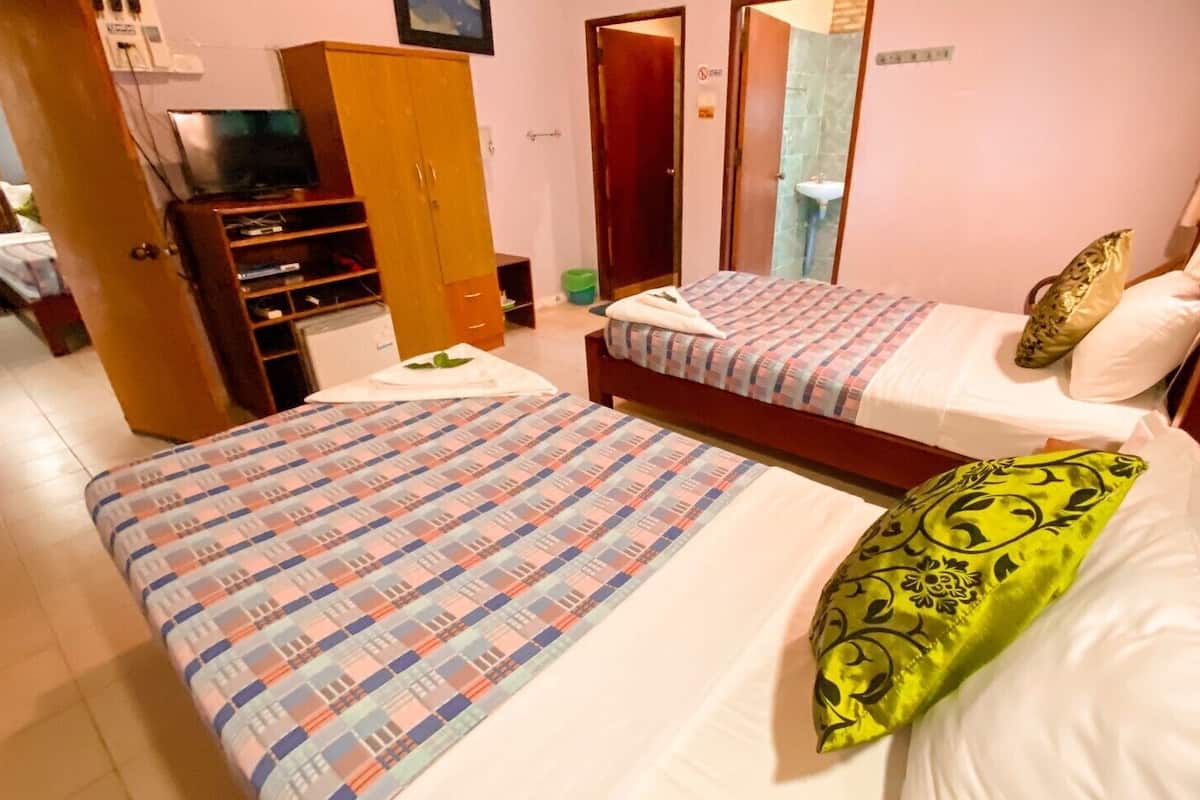 Habitación de hotel con dos camas, un armario, un televisor y un baño visible a través de una puerta abierta.