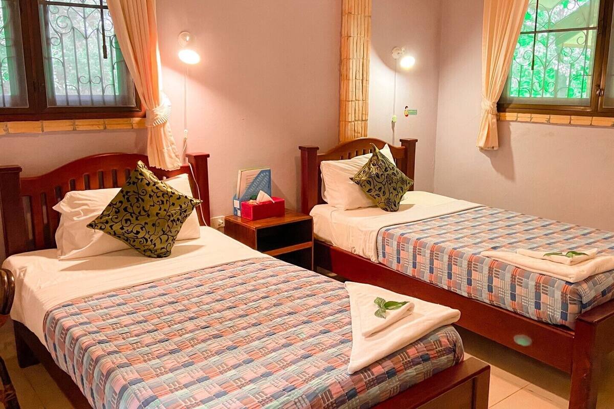 Una habitación con dos camas de madera, cada una con una colcha y almohadas estampadas. Hay mesitas de noche con lámparas y una caja roja pequeña.