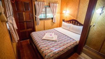 Un dormitorio con cama de madera, ropa de cama escocesa, una ventana con cortinas y una lámpara fijada a la pared.